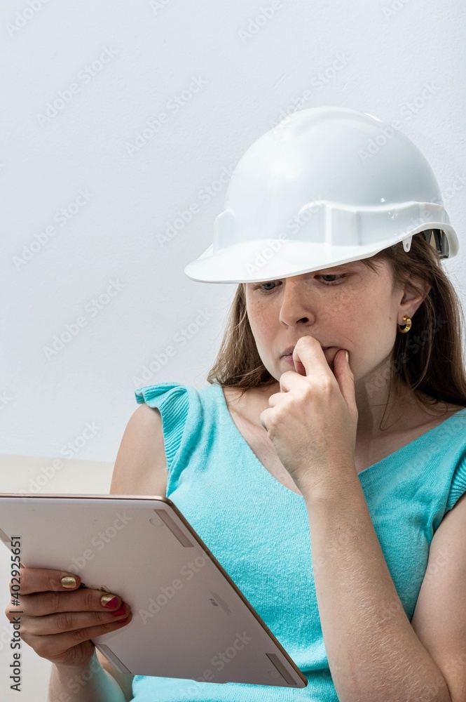 Light-eyed blonde woman with white helmet
of engineer reading a tablet