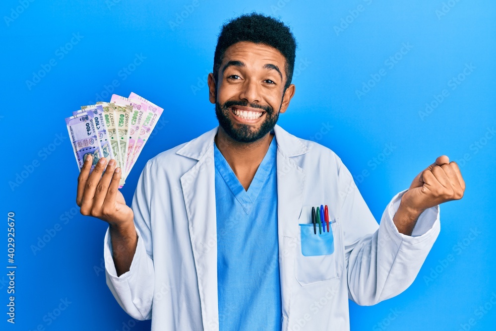 Handsome hispanic man with beard wearing medical uniform holding indian rupee screaming proud, celebrating victory and success very excited with raised arm Handsome hispanic man with beard wearing medical uniform holding indian rupee screaming proud, celebrating victory and success very excited with raised arm