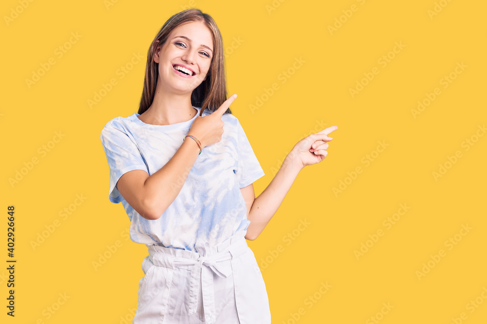 Young beautiful blonde woman wearing tye die tshirt smiling and looking at the camera pointing with two hands and fingers to the side. Young beautiful blonde woman wearing tye die tshirt smiling and looking at the camera pointing with two hands and fingers to the side.