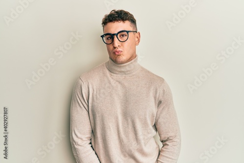 Hispanic young man wearing casual turtleneck sweater looking at the camera blowing a kiss on air being lovely and sexy. love expression. © Krakenimages.com