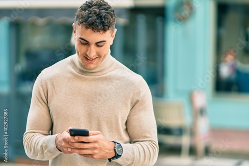 Young hispanic man smiling happy using smartphone at the city.