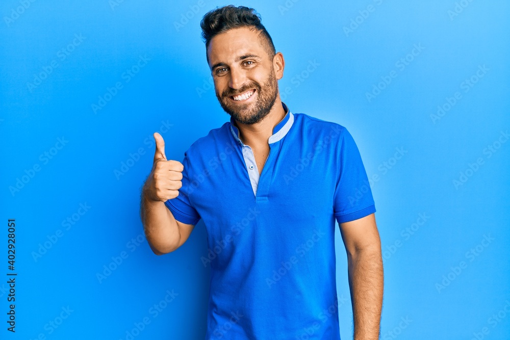 Handsome man with beard wearing casual clothes smiling happy and positive, thumb up doing excellent and approval sign Handsome man with beard wearing casual clothes smiling happy and positive, thumb up doing excellent and approval sign