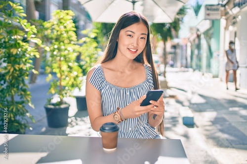 Obraz na plátně Young chinese woman smiling happy sitting on the table at street of city