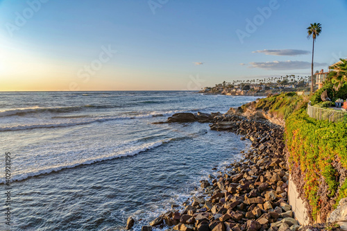 Huge rocks and buildings bordering the tranquil ocean at suset in San Diego CA photo