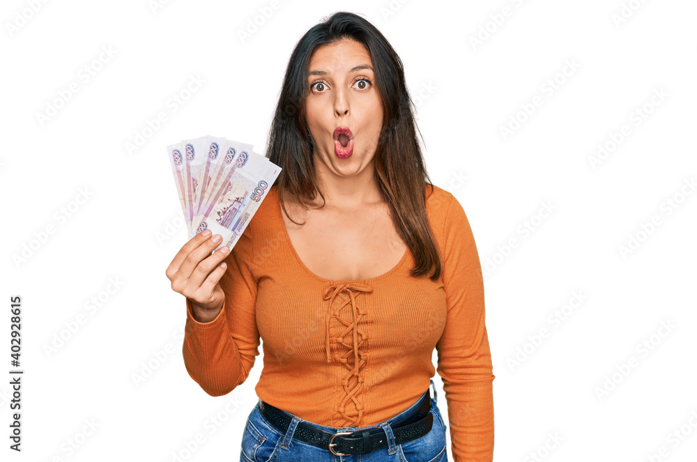 Beautiful hispanic woman holding russian 500 ruble banknotes scared and amazed with open mouth for surprise, disbelief face Beautiful hispanic woman holding russian 500 ruble banknotes scared and amazed with open mouth for surprise, disbelief face