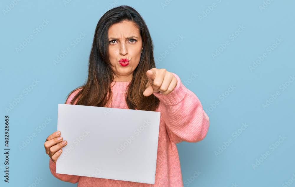 Beautiful hispanic woman holding blank empty banner pointing with finger to the camera and to you, confident gesture looking serious Beautiful hispanic woman holding blank empty banner pointing with finger to the camera and to you, confident gesture looking serious