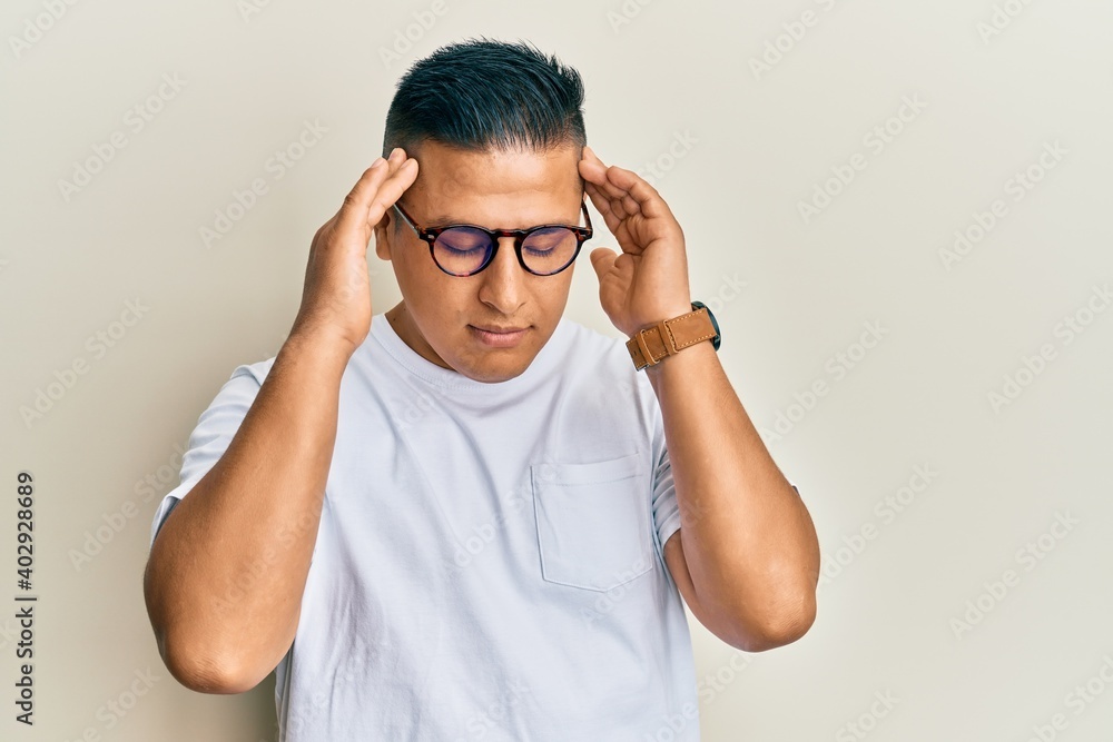 Young latin man wearing casual clothes and glasses with hand on head, headache because stress. suffering migraine. Young latin man wearing casual clothes and glasses with hand on head, headache because stress. suffering migraine.