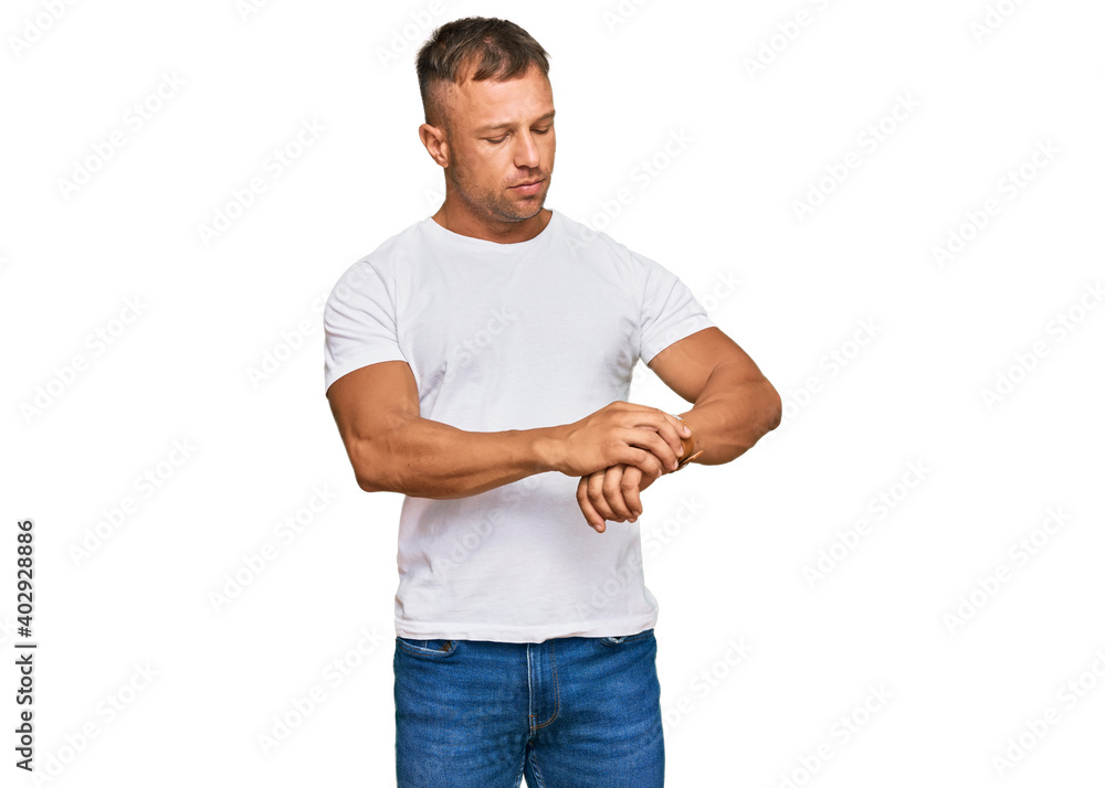 Handsome muscle man wearing casual white tshirt checking the time on wrist watch, relaxed and confident Handsome muscle man wearing casual white tshirt checking the time on wrist watch, relaxed and confident