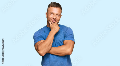 Handsome muscle man wearing casual clothes looking confident at the camera smiling with crossed arms and hand raised on chin. thinking positive.