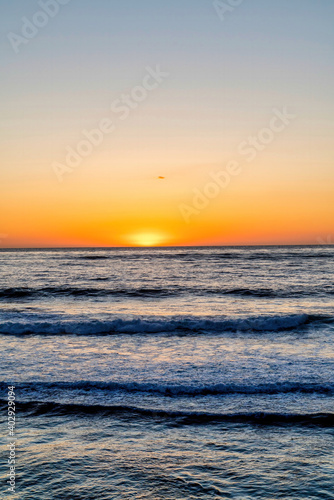 Ocean and waves with orange sun in the horizon in San Diego California at sunset