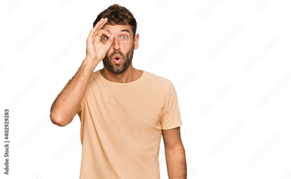Handsome young man with beard wearing casual tshirt doing ok gesture shocked with surprised face, eye looking through fingers. unbelieving expression. Handsome young man with beard wearing casual tshirt doing ok gesture shocked with surprised face, eye looking through fingers. unbelieving expression.