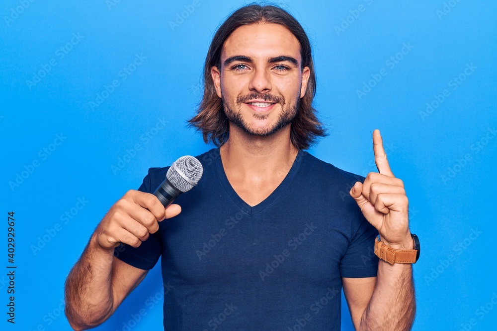 Young handsome man singing song using microphone smiling with an idea or question pointing finger with happy face, number one Young handsome man singing song using microphone smiling with an idea or question pointing finger with happy face, number one