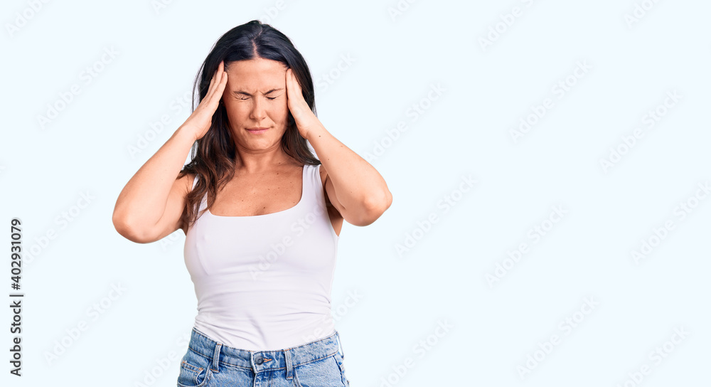 Young beautiful brunette woman wearing casual sleeveless t-shirt with hand on head for pain in head because stress. suffering migraine. Young beautiful brunette woman wearing casual sleeveless t-shirt with hand on head for pain in head because stress. suffering migraine.
