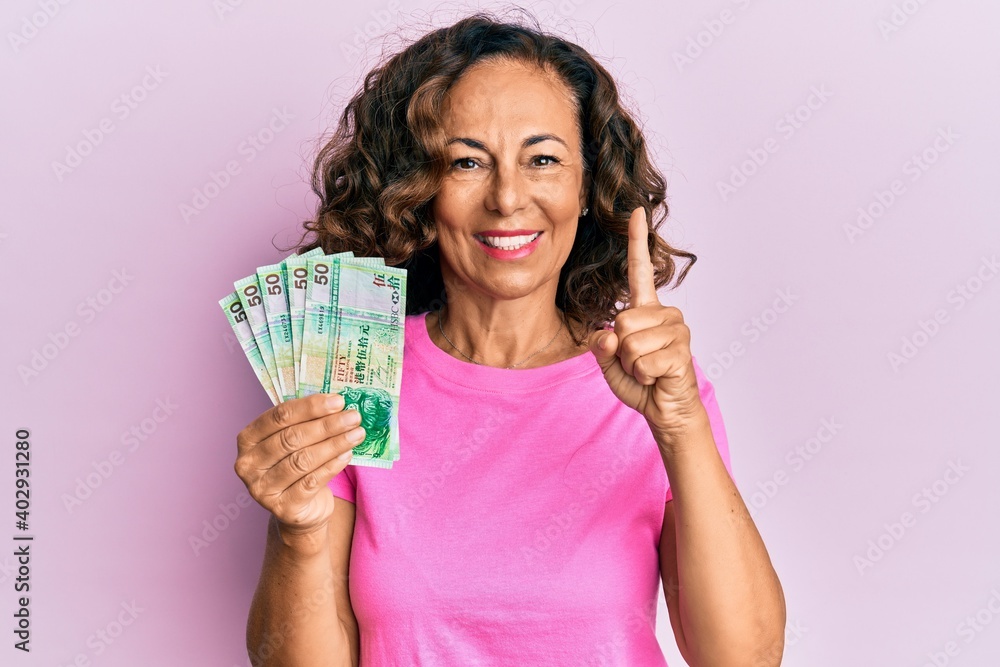 Middle age hispanic woman holding 50 hong kong dollars banknotes smiling with an idea or question pointing finger with happy face, number one Middle age hispanic woman holding 50 hong kong dollars banknotes smiling with an idea or question pointing finger with happy face, number one