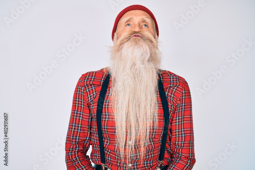 Old senior man with grey hair and long beard wearing hipster look with wool cap looking at the camera blowing a kiss on air being lovely and sexy. love expression.
