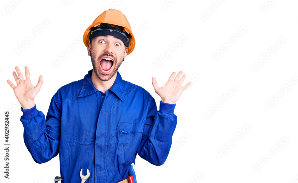 Young hispanic man wearing worker uniform celebrating crazy and amazed for success with arms raised and open eyes screaming excited. winner concept