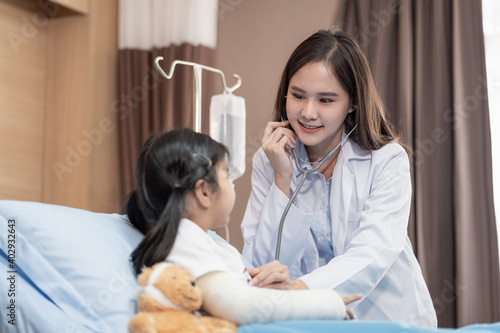Fototapeta Naklejka Na Ścianę i Meble -  Young smiling female pediatrician doctor and child patient with a teddy bear in the health medical center, talking positively with the kid for the encouragement