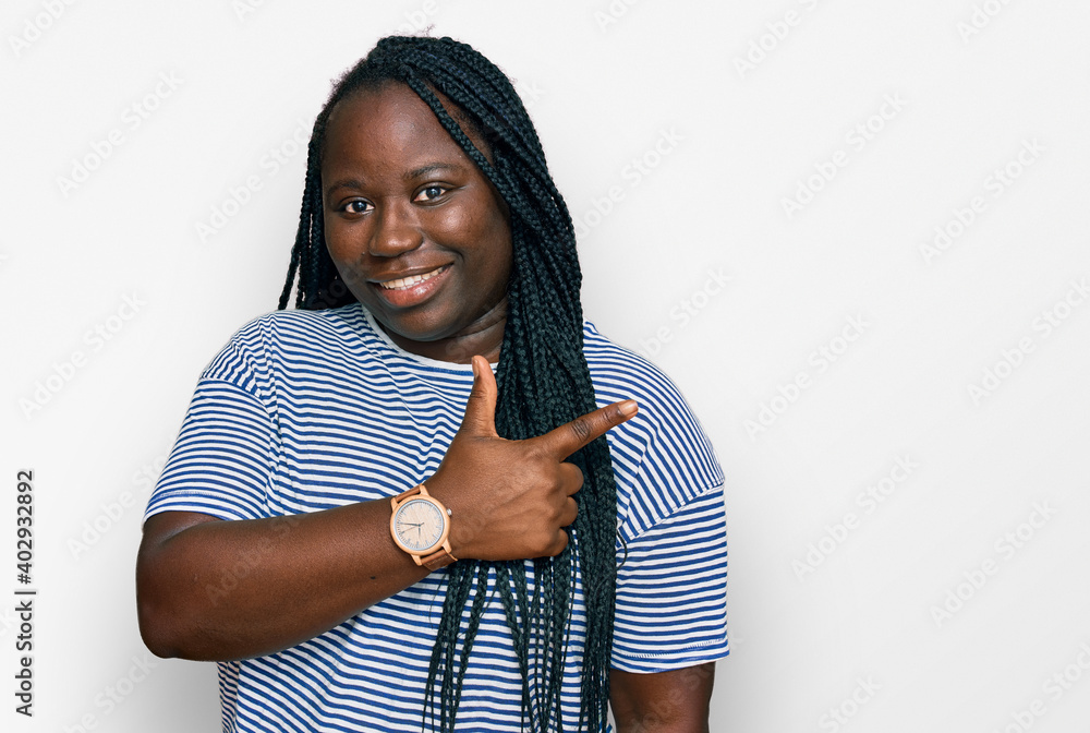 Young black woman with braids wearing casual clothes cheerful with a smile of face pointing with hand and finger up to the side with happy and natural expression on face Young black woman with braids wearing casual clothes cheerful with a smile of face pointing with hand and finger up to the side with happy and natural expression on face