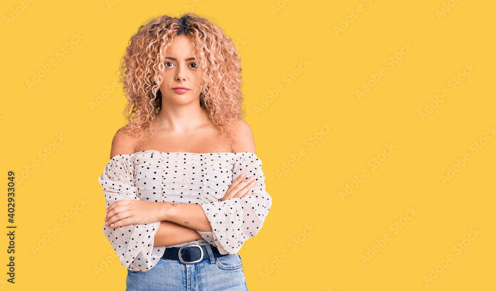Young blonde woman with curly hair wearing casual clothes skeptic and nervous, disapproving expression on face with crossed arms. negative person. Young blonde woman with curly hair wearing casual clothes skeptic and nervous, disapproving expression on face with crossed arms. negative person.