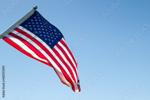 American Flag And Blue Sky. Sunlight shines on the American Flag set against a blue sky in horizontal orientation with copy space. 