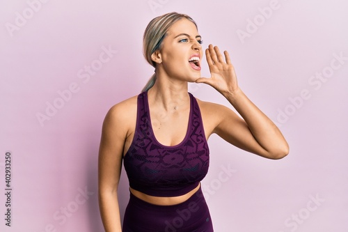 Beautiful blonde woman wearing sportswear over pink background shouting and screaming loud to side with hand on mouth. communication concept.
