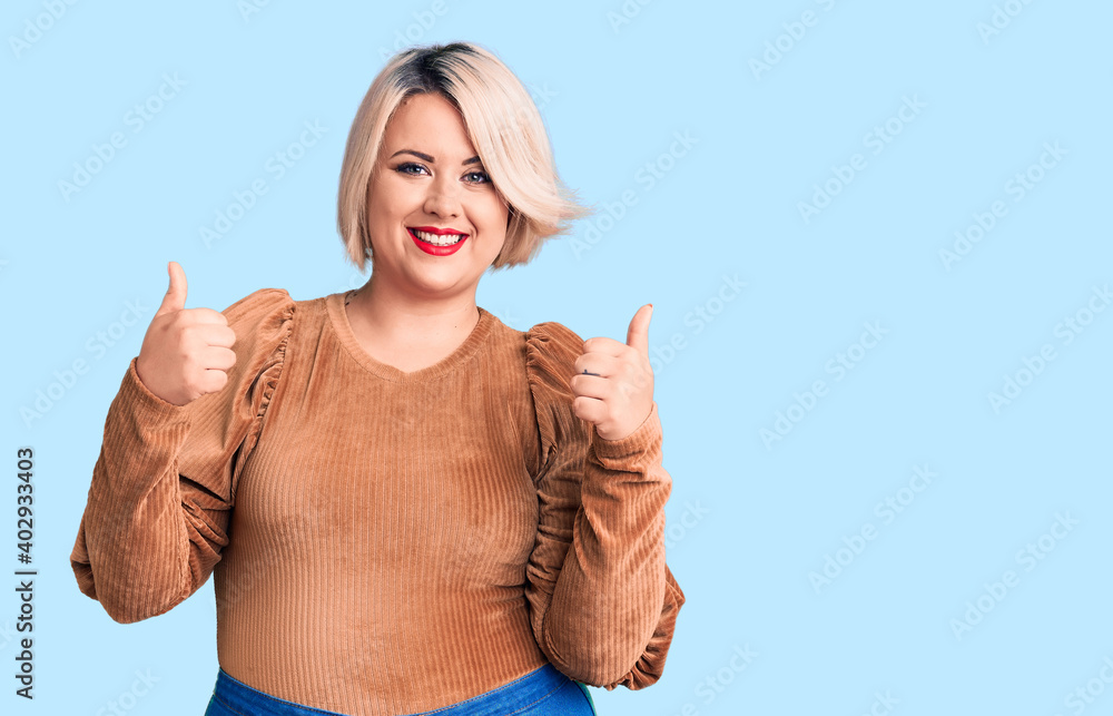 Young blonde plus size woman wearing casual sweater success sign doing positive gesture with hand, thumbs up smiling and happy. cheerful expression and winner gesture.