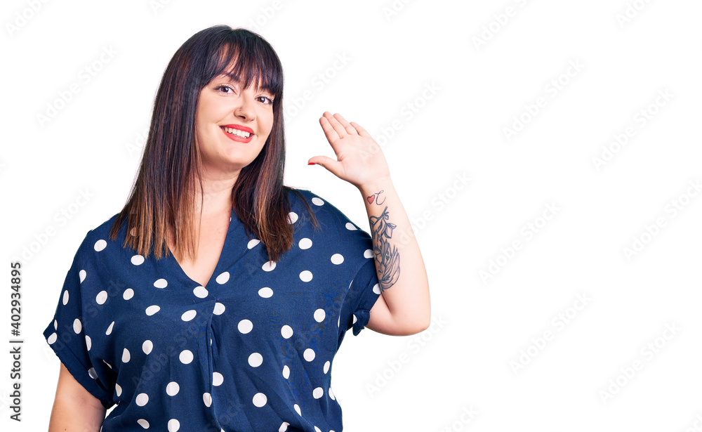 Young plus size woman wearing casual clothes waiving saying hello happy and smiling, friendly welcome gesture Young plus size woman wearing casual clothes waiving saying hello happy and smiling, friendly welcome gesture