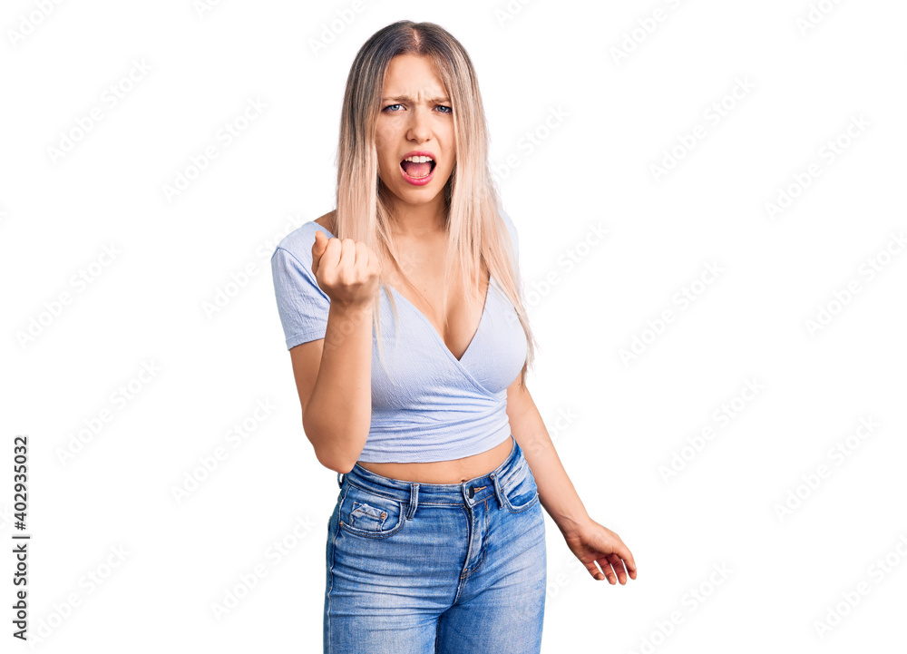 Young beautiful blonde woman wearing casual clothes angry and mad raising fist frustrated and furious while shouting with anger. rage and aggressive concept. Young beautiful blonde woman wearing casual clothes angry and mad raising fist frustrated and furious while shouting with anger. rage and aggressive concept.