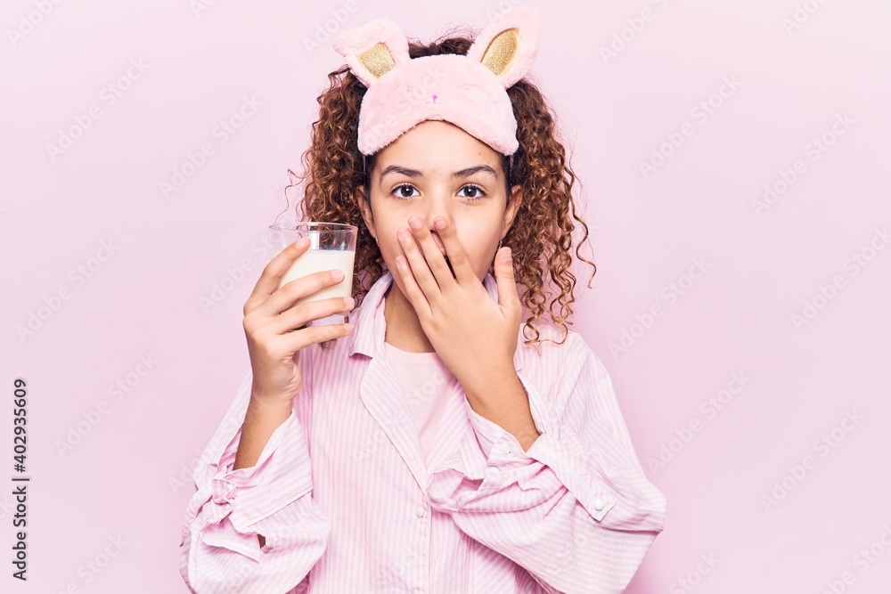 Beautiful kid girl with curly hair wearing sleep mask and pajama holding milk covering mouth with hand, shocked and afraid for mistake. surprised expression Beautiful kid girl with curly hair wearing sleep mask and pajama holding milk covering mouth with hand, shocked and afraid for mistake. surprised expression