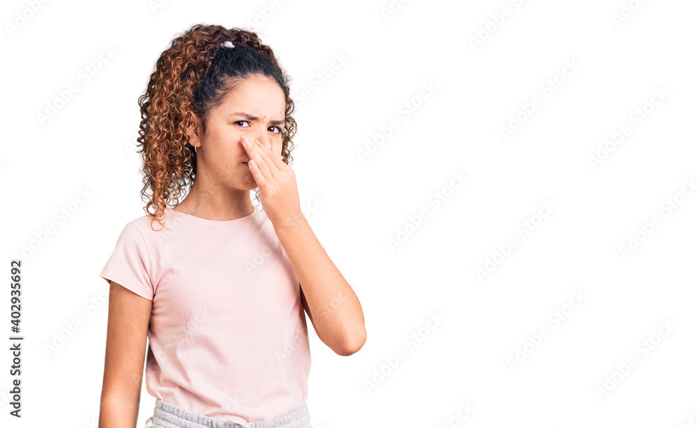 Beautiful kid girl with curly hair wearing casual clothes smelling something stinky and disgusting, intolerable smell, holding breath with fingers on nose. bad smell Beautiful kid girl with curly hair wearing casual clothes smelling something stinky and disgusting, intolerable smell, holding breath with fingers on nose. bad smell