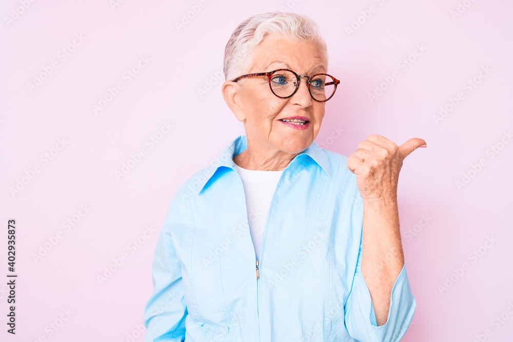 Senior beautiful woman with blue eyes and grey hair wearing glasses smiling with happy face looking and pointing to the side with thumb up. Senior beautiful woman with blue eyes and grey hair wearing glasses smiling with happy face looking and pointing to the side with thumb up.