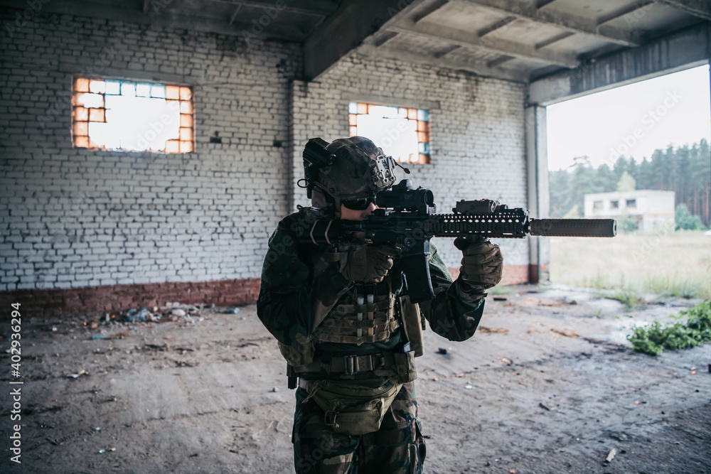 Fototapeta premium Soldier in full US MARSOC armed with assault rifle run through the abandoned building. Military clash.