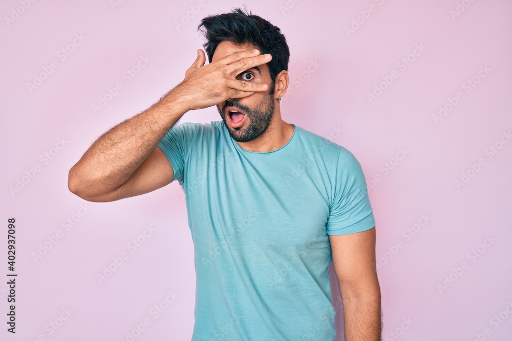 Handsome hispanic man with beard wearing casual clothes peeking in shock covering face and eyes with hand, looking through fingers with embarrassed expression. Handsome hispanic man with beard wearing casual clothes peeking in shock covering face and eyes with hand, looking through fingers with embarrassed expression.