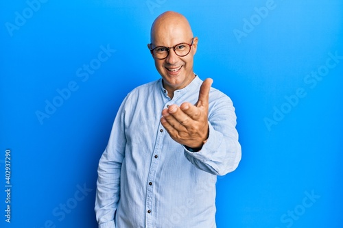 Middle age bald man wearing casual clothes and glasses smiling friendly offering handshake as greeting and welcoming. successful business.