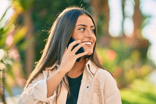 Young hispanic girl smiling happy talking on the smartphone at the park.