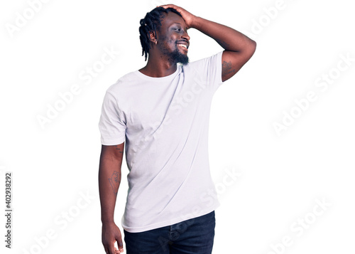 Young african american man with braids wearing casual white tshirt smiling confident touching hair with hand up gesture, posing attractive and fashionable