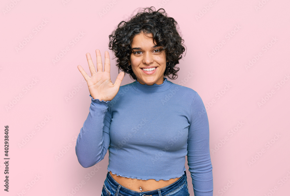 Young hispanic woman with curly hair wearing casual clothes showing and pointing up with fingers number five while smiling confident and happy. - obrazy, fototapety, plakaty 