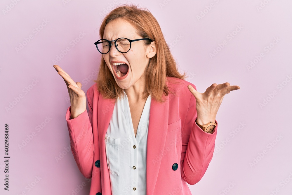 Young caucasian woman wearing business style and glasses celebrating mad and crazy for success with arms raised and closed eyes screaming excited. winner concept Young caucasian woman wearing business style and glasses celebrating mad and crazy for success with arms raised and closed eyes screaming excited. winner concept