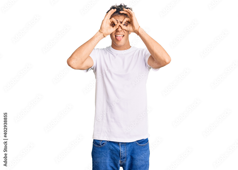 Young handsome man wearing casual white tshirt doing ok gesture like binoculars sticking tongue out, eyes looking through fingers. crazy expression. Young handsome man wearing casual white tshirt doing ok gesture like binoculars sticking tongue out, eyes looking through fingers. crazy expression.
