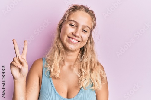 Young blonde girl wearing casual clothes showing and pointing up with fingers number two while smiling confident and happy.