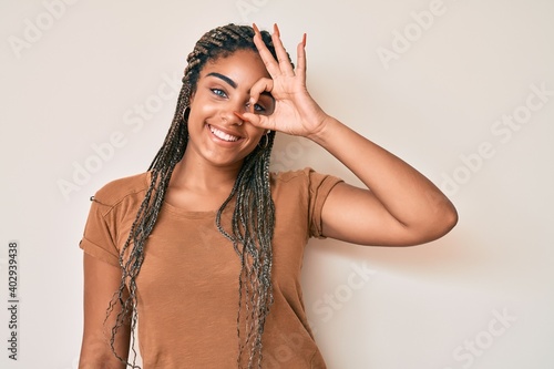 Young african american woman with braids wearing casual clothes smiling happy doing ok sign with hand on eye looking through fingers