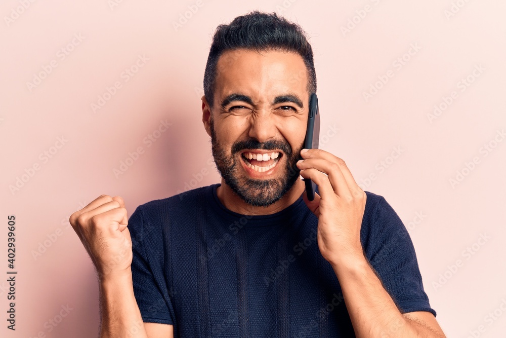Young hispanic man having conversation talking on the smartphone screaming proud, celebrating victory and success very excited with raised arm Young hispanic man having conversation talking on the smartphone screaming proud, celebrating victory and success very excited with raised arm