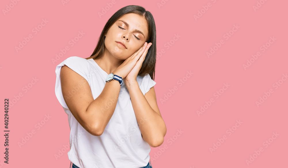 Young caucasian woman wearing casual white tshirt sleeping tired dreaming and posing with hands together while smiling with closed eyes. Young caucasian woman wearing casual white tshirt sleeping tired dreaming and posing with hands together while smiling with closed eyes.
