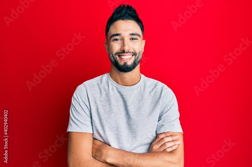 Young man with beard wearing casual white tshirt happy face smiling with crossed arms looking at the camera. positive person. © Krakenimages.com