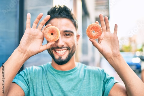 Young arab man smiling happy holding small donuts over eye at the city. photo