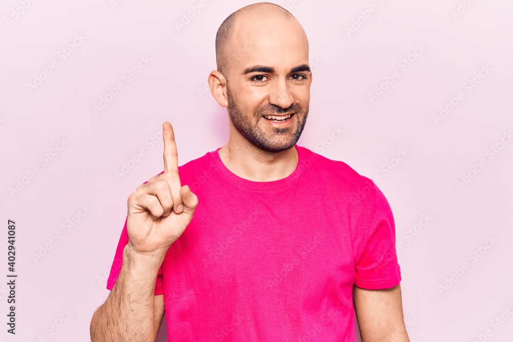 Young handsome bald man wearing casual t shirt smiling with an idea or question pointing finger up with happy face, number one Young handsome bald man wearing casual t shirt smiling with an idea or question pointing finger up with happy face, number one