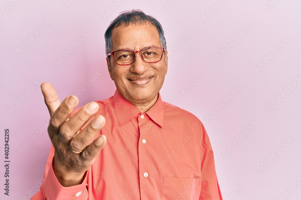 Middle age indian man wearing casual clothes and glasses smiling friendly offering handshake as greeting and welcoming. successful business. Middle age indian man wearing casual clothes and glasses smiling friendly offering handshake as greeting and welcoming. successful business.