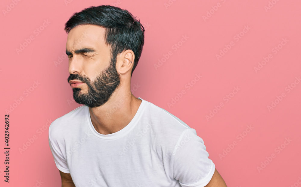 Young hispanic man wearing casual white t shirt with hand on stomach because nausea, painful disease feeling unwell. ache concept. Young hispanic man wearing casual white t shirt with hand on stomach because nausea, painful disease feeling unwell. ache concept.