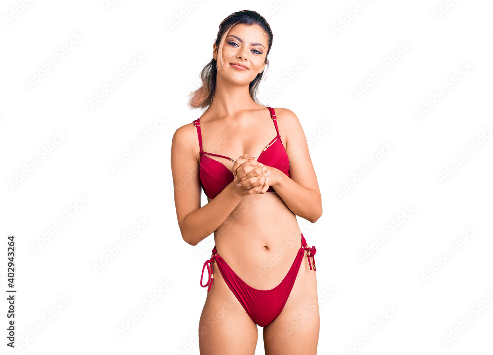 Fototapeta premium Young beautiful woman wearing bikini with hands together and crossed fingers smiling relaxed and cheerful. success and optimistic