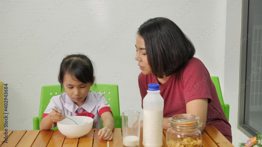 Asian family Mother Prepare breakfast cornflakes with milk for daughter In the morning before go to school of Thai families in their daily life. Asian family Mother Prepare breakfast cornflakes with milk for daughter In the morning before go to school of Thai families in their daily life.